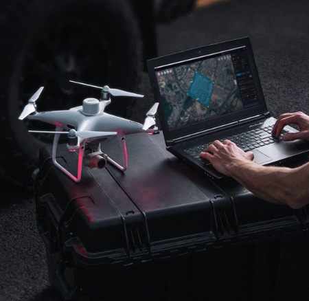 eine Person benutzt einen Laptop, neben dem eine Drohne steht