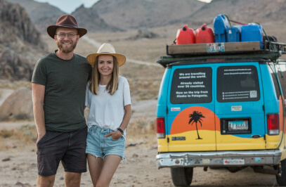 Ein Paar posiert für ein Urlaubsfoto in der Natur, neben einem bunten Geländewagen