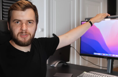 Mann spricht in die Kamera, sitzt am Schreibtisch und hält eine Lampe auf den Monitor